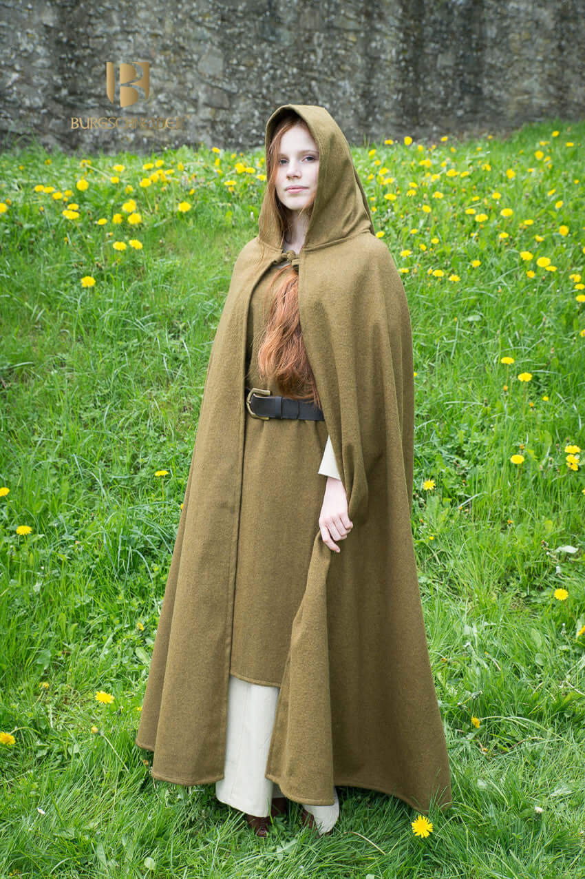 Wool Hooded Cloak Hibernus in Autumn Green worn by a model in a grassy field with flowers.