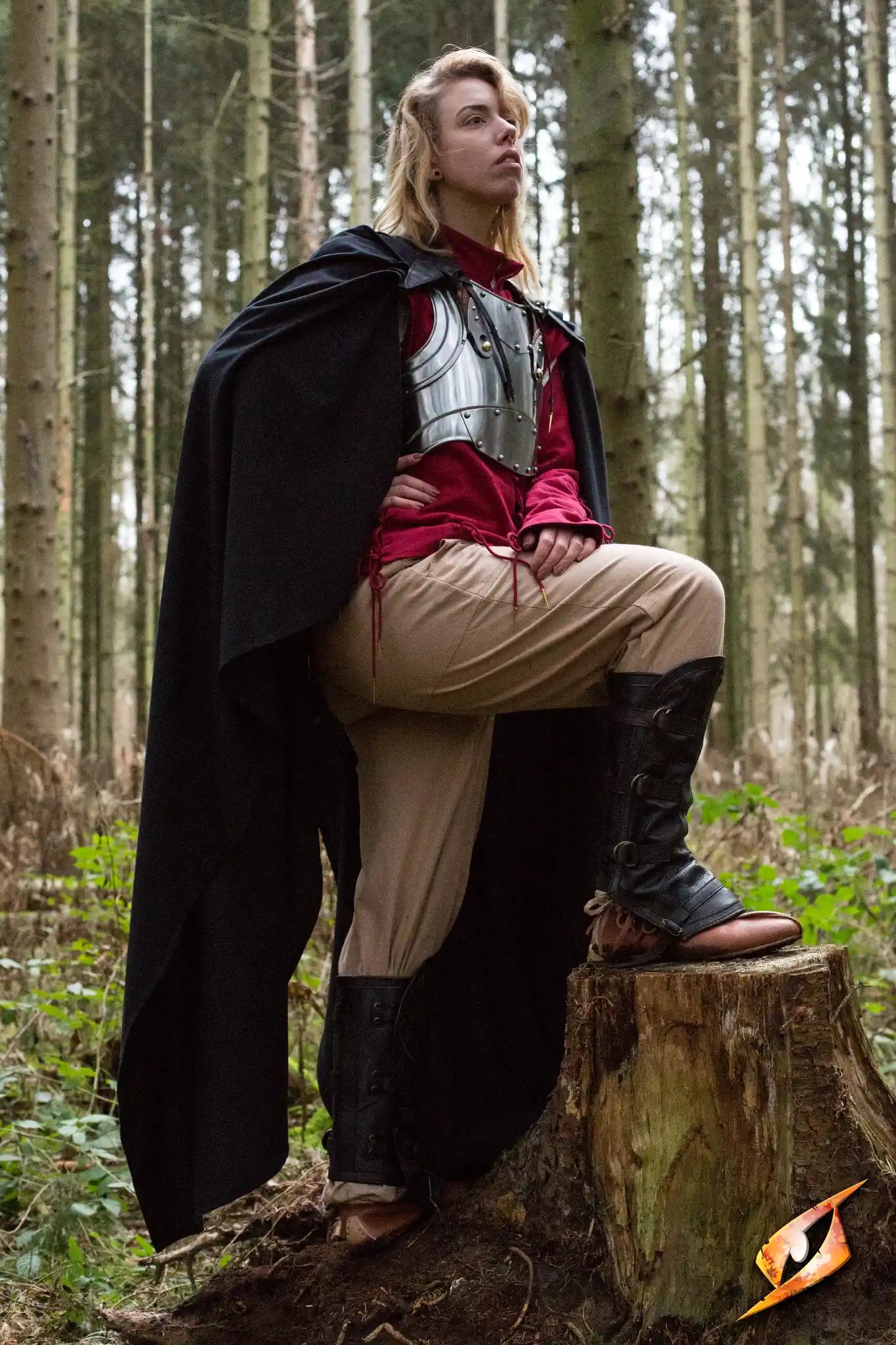 Person wearing the Cape Regulus standing on a tree stump in a forest, showcasing the stunning black cape and armor.