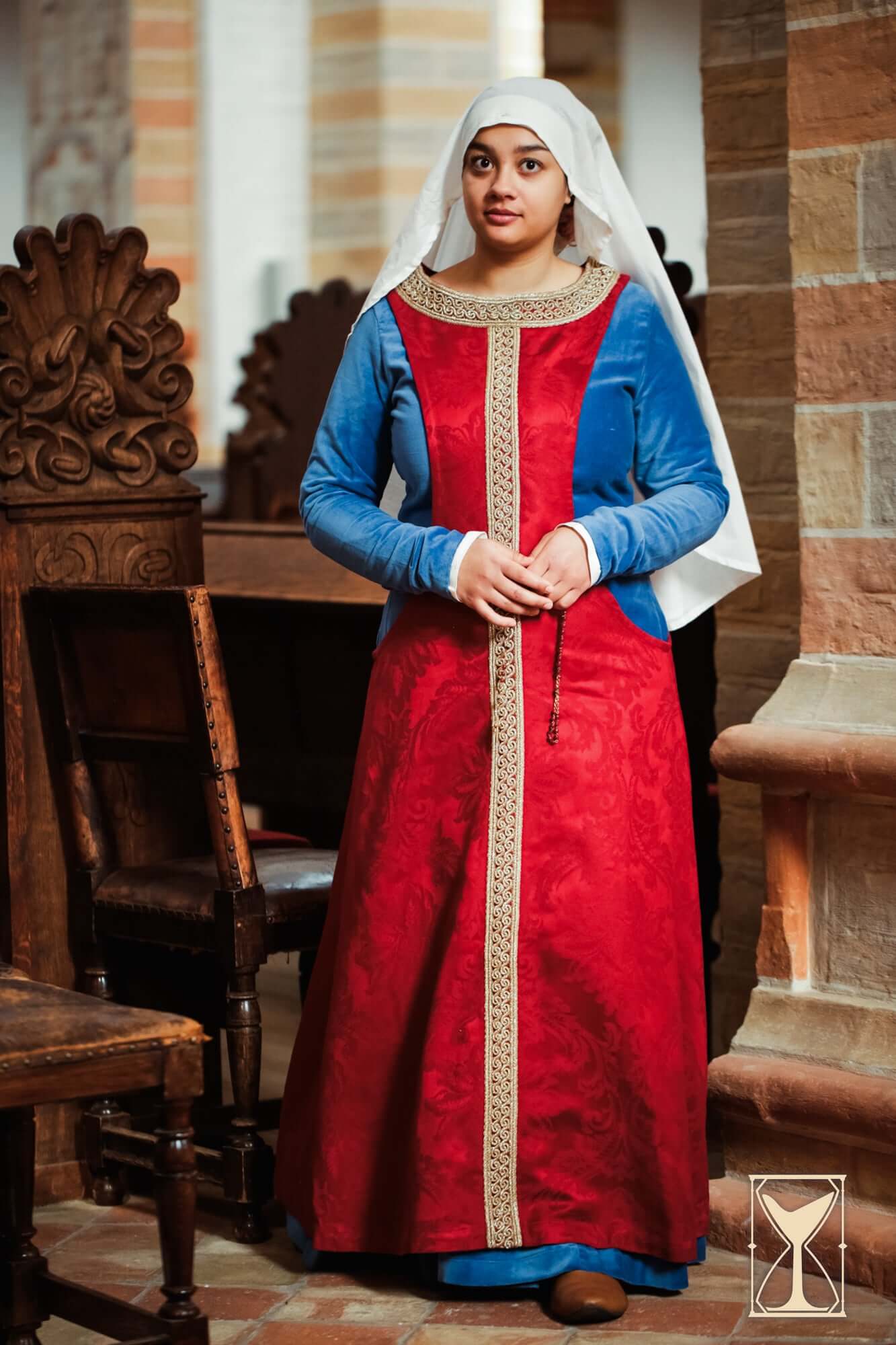 Pellote - Medieval Dress worn by a woman, showcasing the deep side openings and elegant brocade fabric in red and blue.