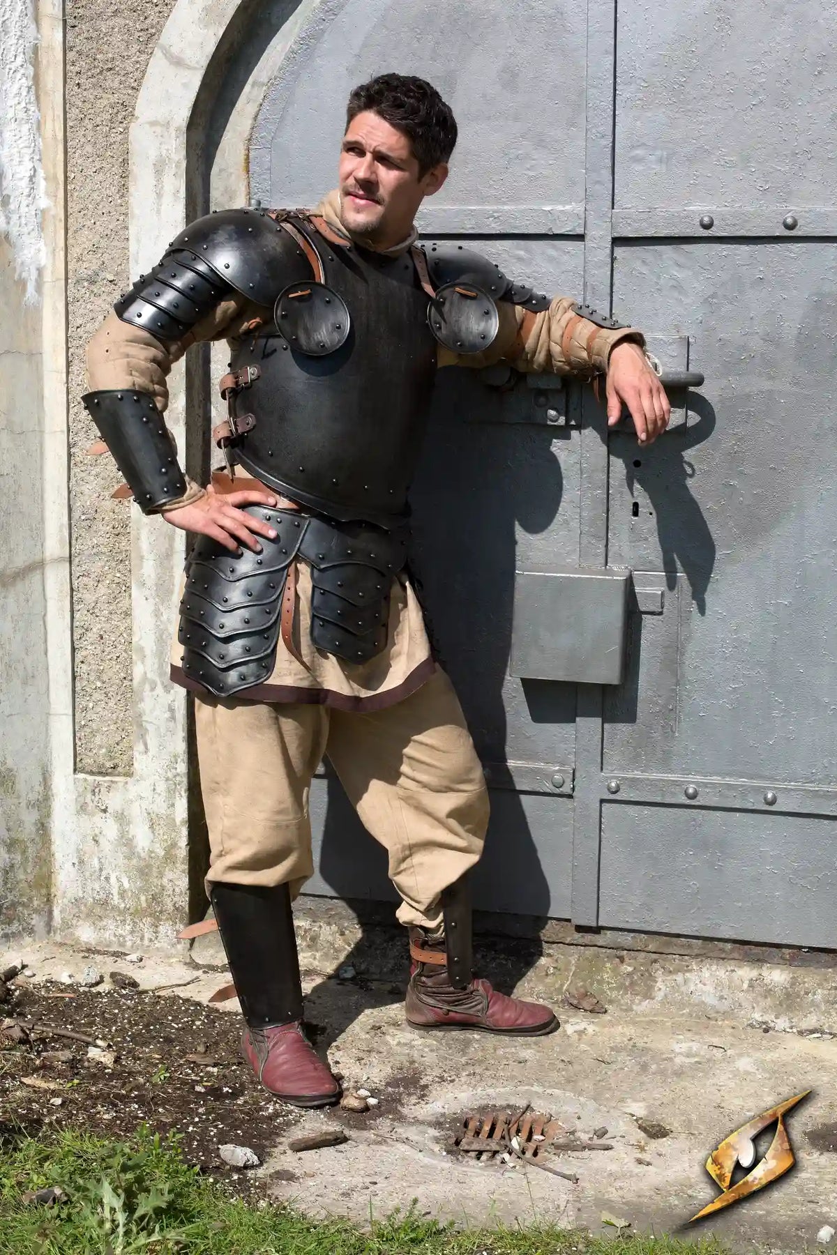 Warrior Complete Armour set worn by a man posing confidently in front of a medieval door with a dark color theme.