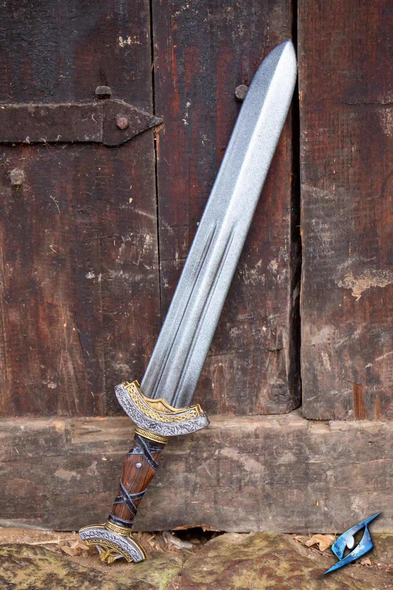 Warlord Sword resting against a wooden door, showcasing its ornate handle and double fuller blade design.