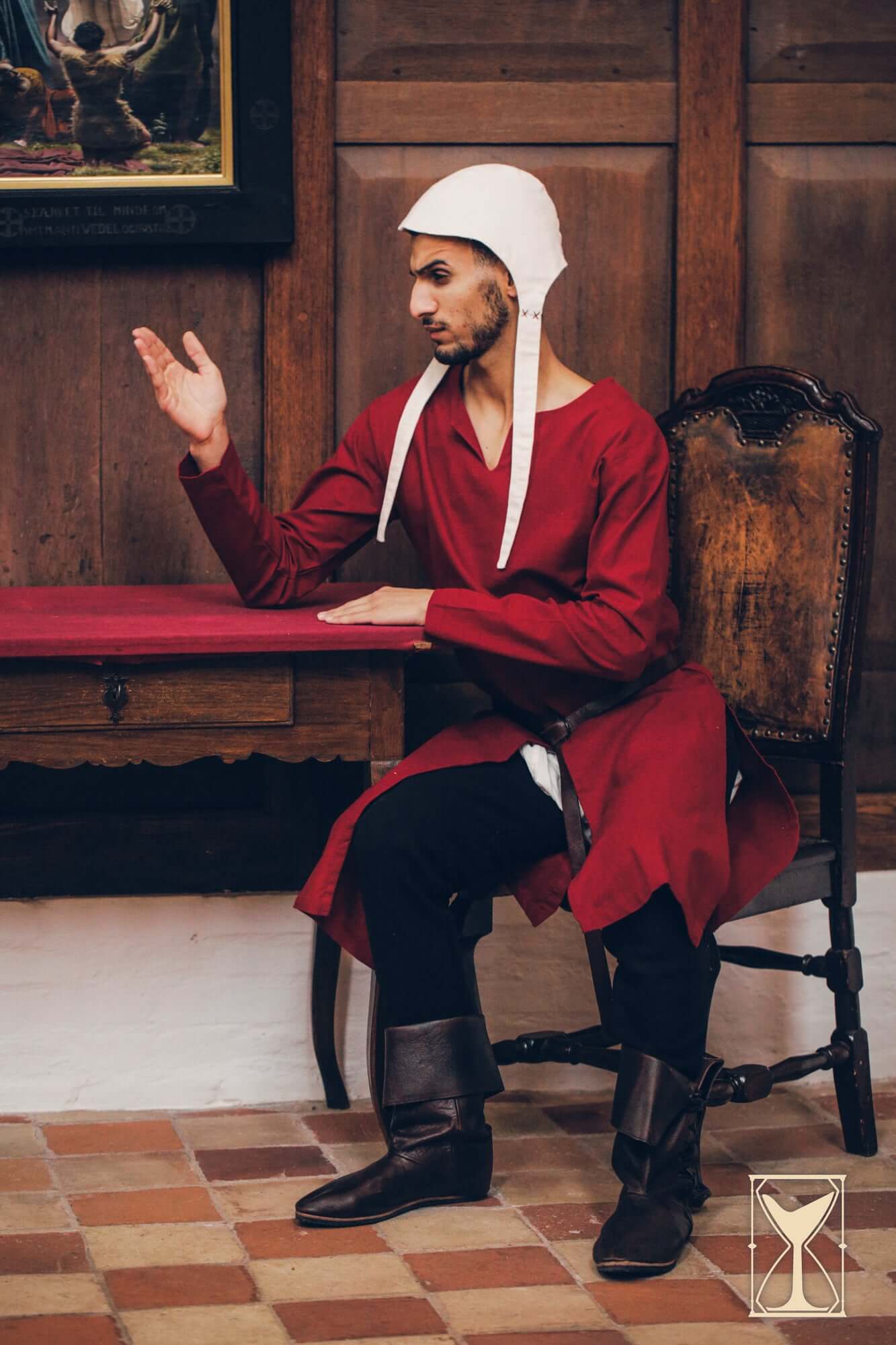 Medieval Riding Tunic worn by a model sitting at a table, showcasing its classic design and functionality.