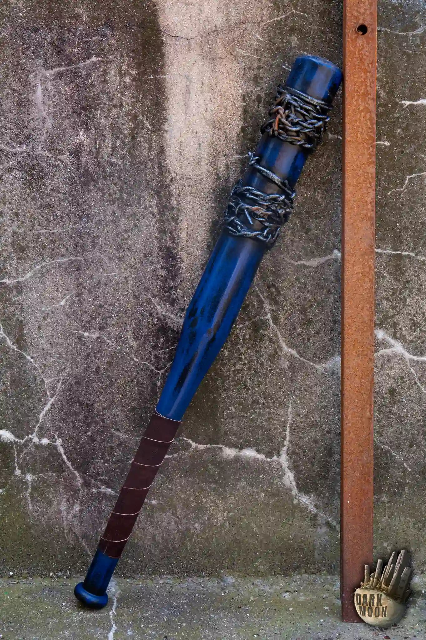 Barbed Wire Bat leaning against a rusty metal pole, featuring blue paint and barbed wire design.