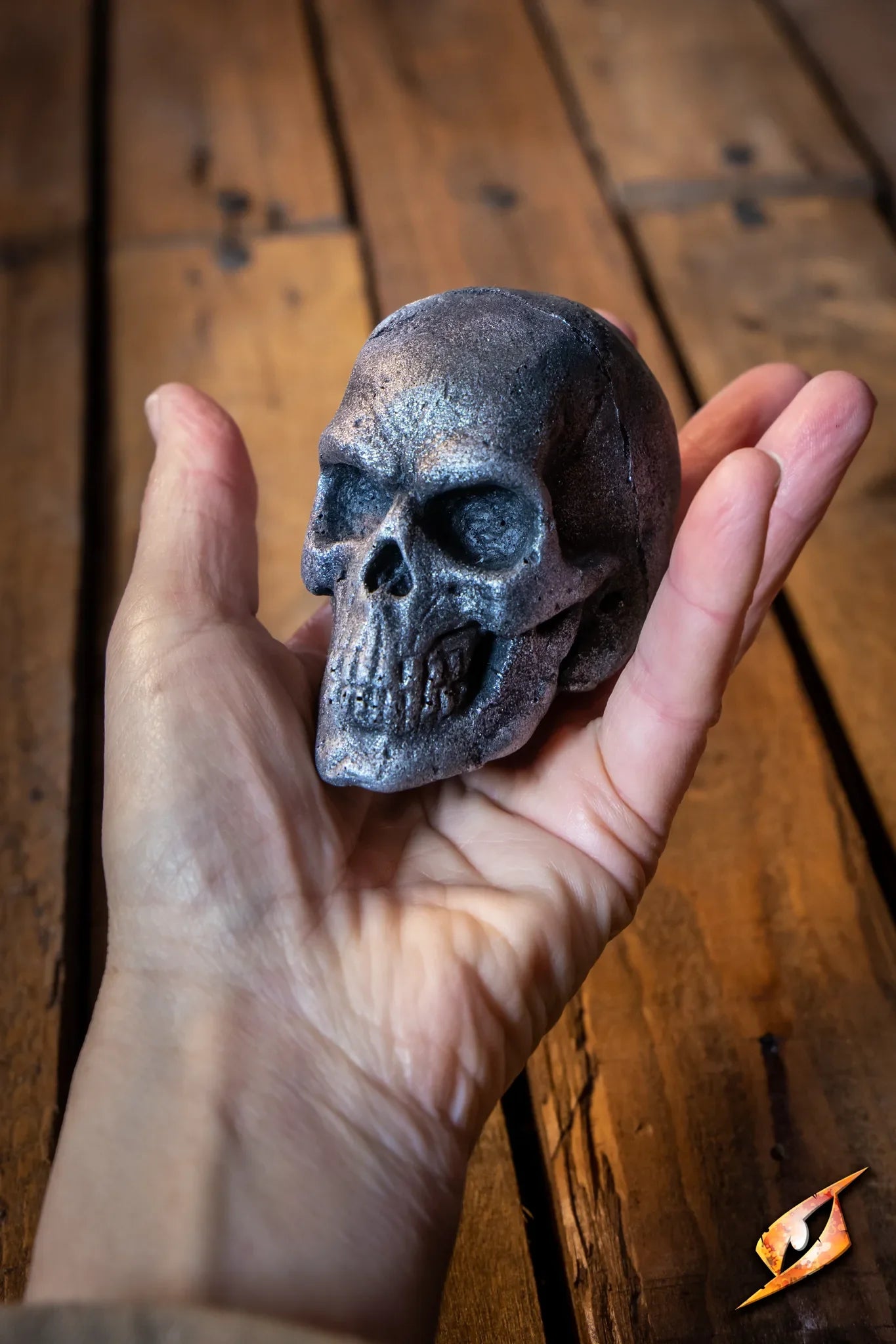 A hand holding a Small Skull on a wooden surface, symbolizing power and magic for orc shamans.