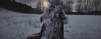 Knight in steel plate armor and helmet in a snowy winter landscape, holding a sword and wearing medieval gauntlets and a red wool cloak. Filmed outdoors in cold weather. 